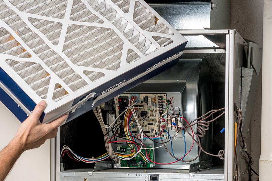 Hand replacing an HVAC air filter next to an exposed control board